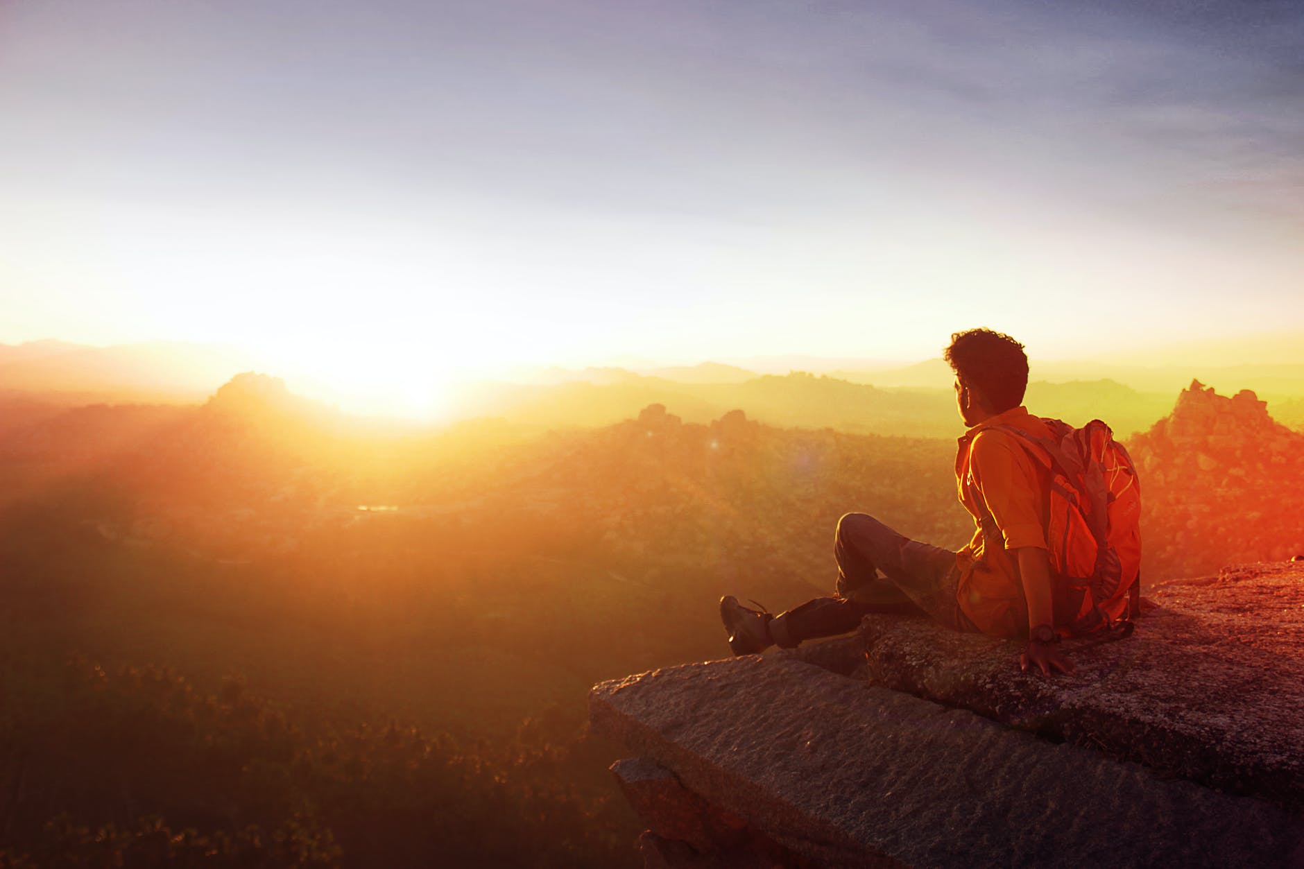 man sitting on edge facing sunset