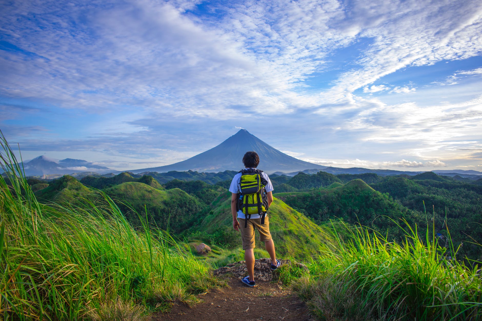 man wearing white shirt brown shorts and green backpack standing on hill